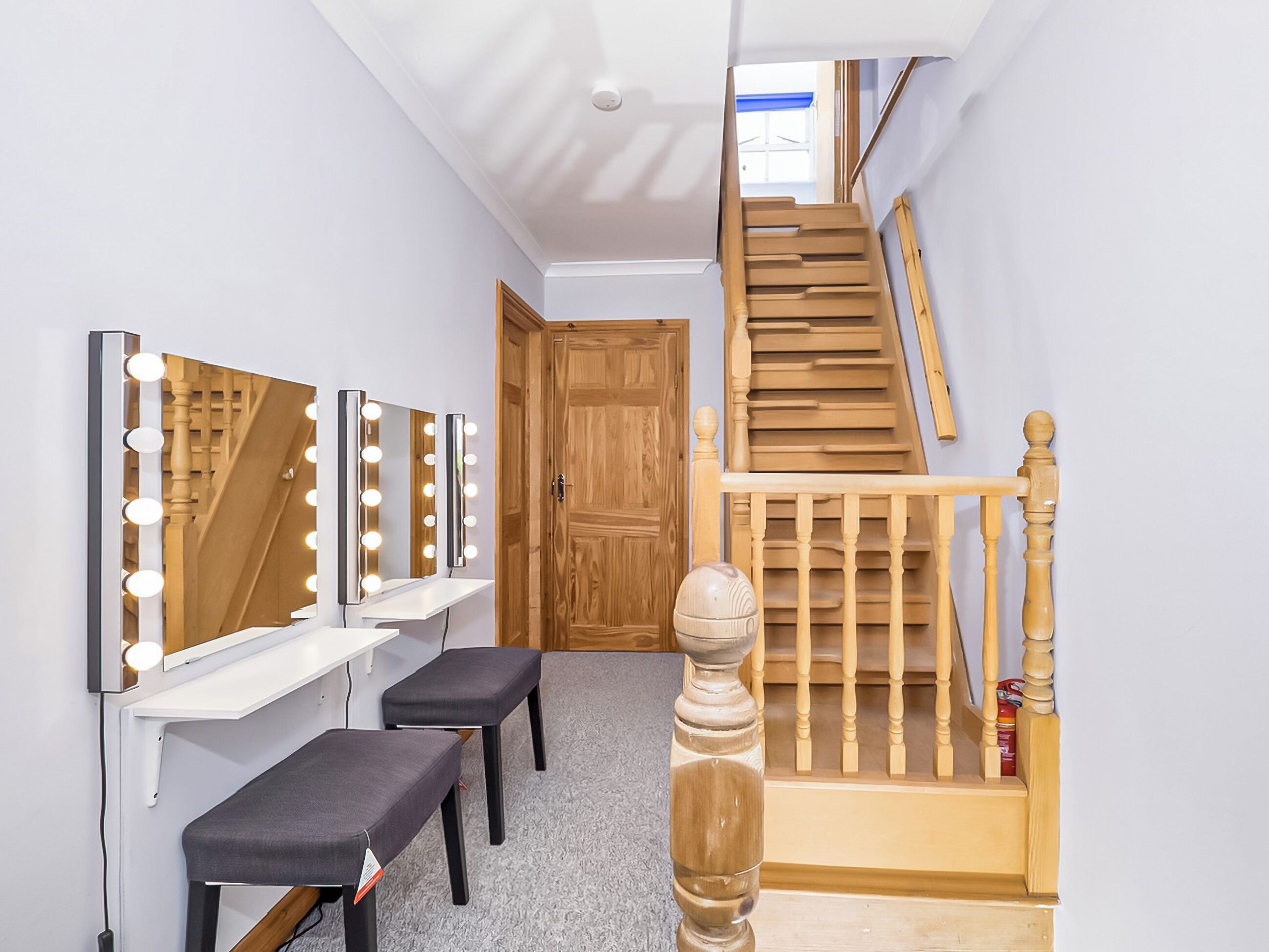 Un corridoio con un angolo toilette dotato di specchi e illuminazione, una scala in legno e una porta che conduce in un'altra stanza.