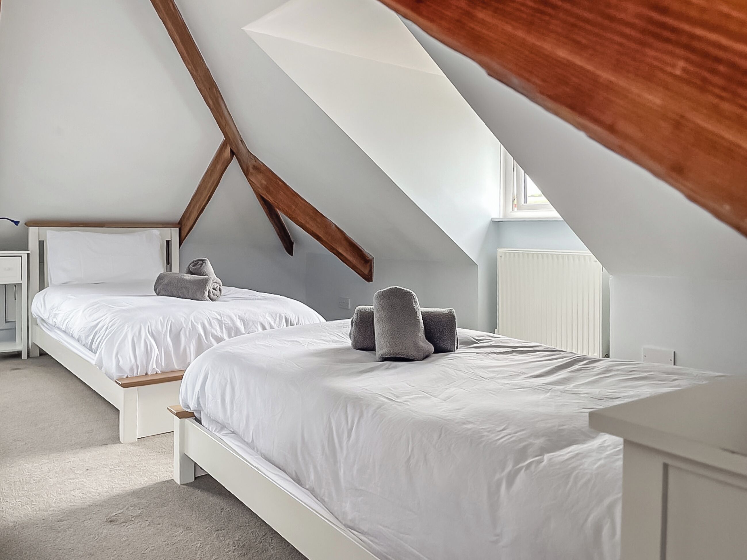 Un dormitorio con dos camas, vigas de madera, un radiador blanco y una ventana.