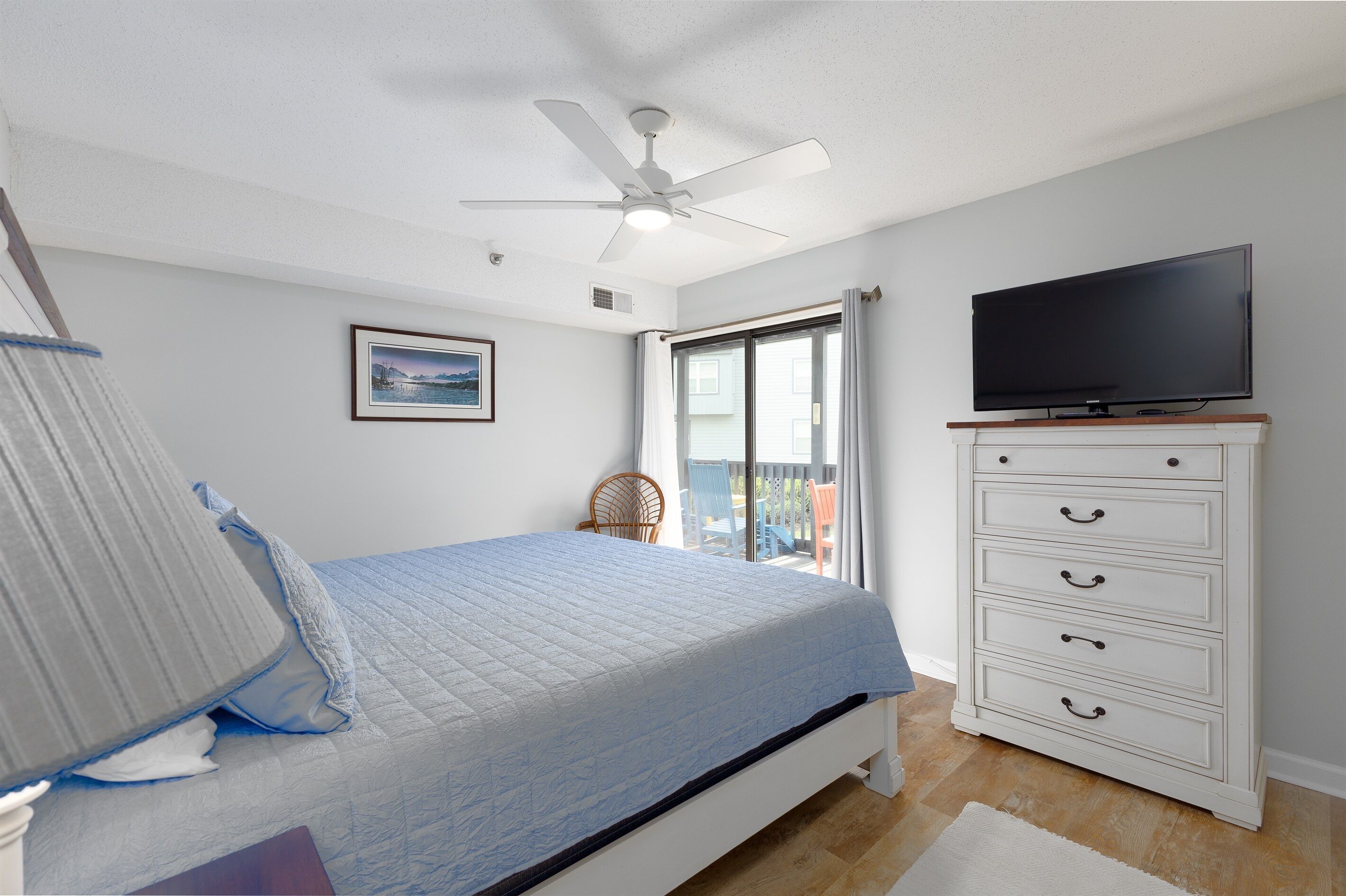 A bedroom with a bed, a television on a dresser, a ceiling fan, and a window with curtains.