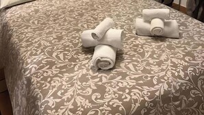 Habitación de hotel con una cama grande, dos toallas enrolladas sobre la cama, un cuadro en la pared, una lámpara y un armario.