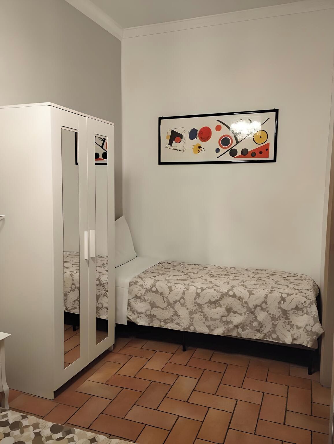 Ein Schlafzimmer mit einem Bett, einem Kleiderschrank, einem Spiegel und einem an der Wand hängenden abstrakten Gemälde.