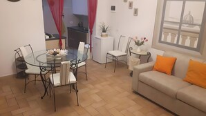 Una sala de estar con una mesa de comedor de vidrio, sofá blanco y vista a un edificio a través de una ventana.