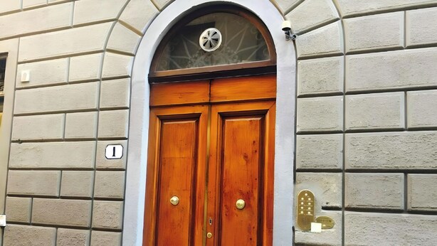 Puerta doble de madera con manija de bronce, incrustada en una pared de ladrillo que tiene un pequeño ventanal arriba.
