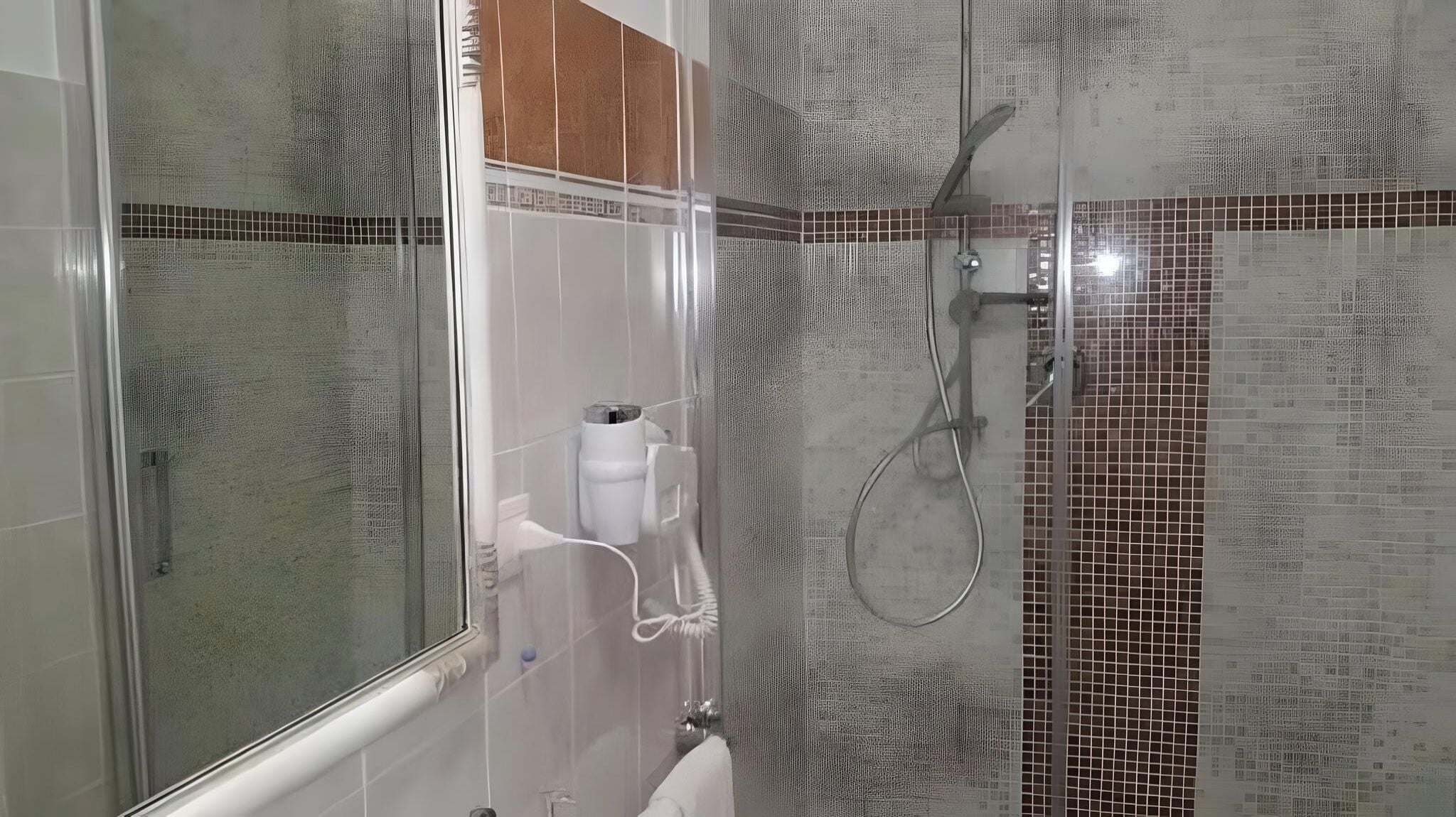 A bathroom with a glass shower enclosure, a white toilet, and a tiled wall with a pattern.