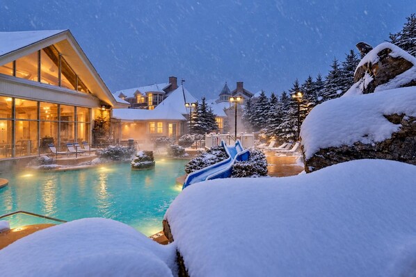 Un resort con piscina climatizada, sillas de descanso y árboles cubiertos de nieve.