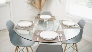 Mesa de comedor preparada para cuatro personas, con copas y platos de vidrio, rodeada de sillas grises.