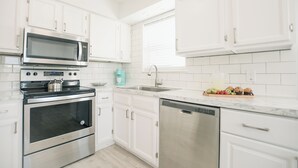 Cocina moderna con armarios blancos, electrodomésticos de acero inoxidable y encimera de mármol.