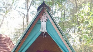 A triangular tent with a sleeping area, a macrame decoration, and a brown blanket. - Aqui no Camping (Brumadinho)