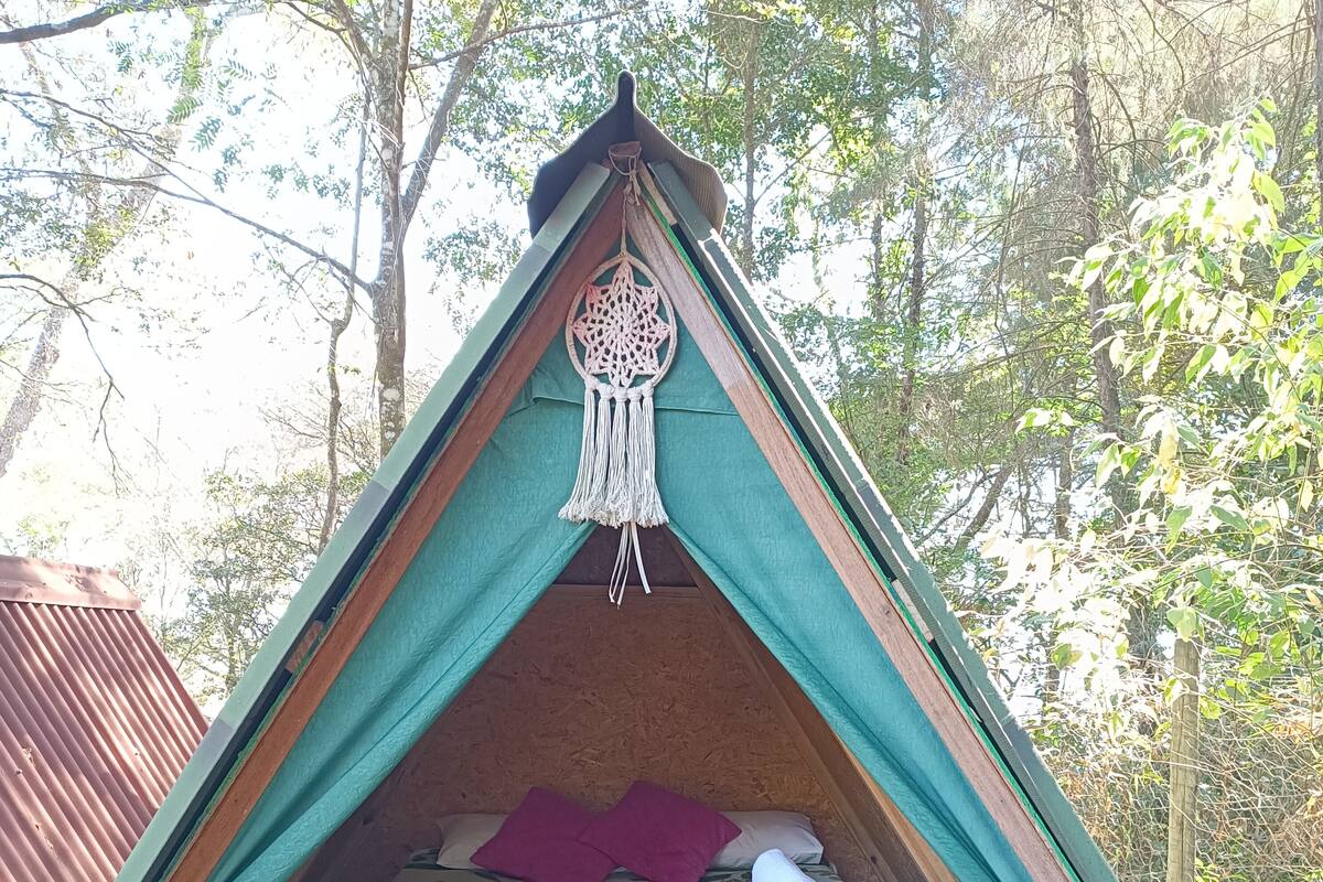 Tienda triangular con zona de dormir, decoración de macramé y manta marrón.