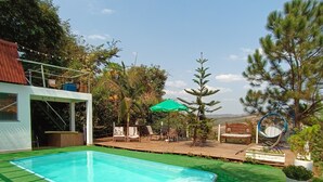A swimming pool with a green deck, surrounded by outdoor furniture and potted plants. - Aqui no Camping (Brumadinho)