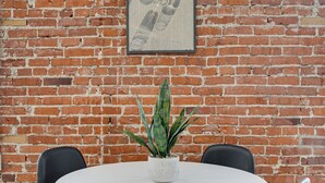 Een ronde tafel met vier zwarte stoelen, een potplant en een lijst met een foto aan een bakstenen muur.