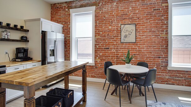 Een keuken met een houten tafel, stoelen, een koelkast en een bakstenen muur.