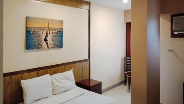 Habitación de hotel con cama, mesita de noche, un cuadro de veleros y un televisor en la pared.