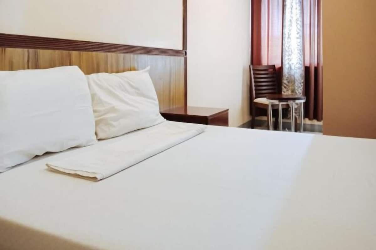 A neatly made bed with white linens, a wooden headboard, a small bedside table, and a chair with a metal frame.