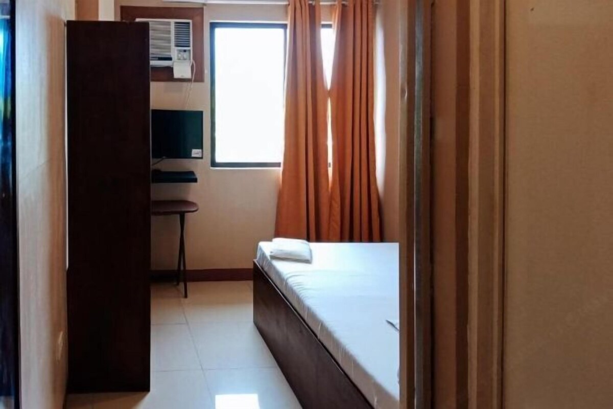 A room with a bed, a desk, a chair, and a window with curtains.