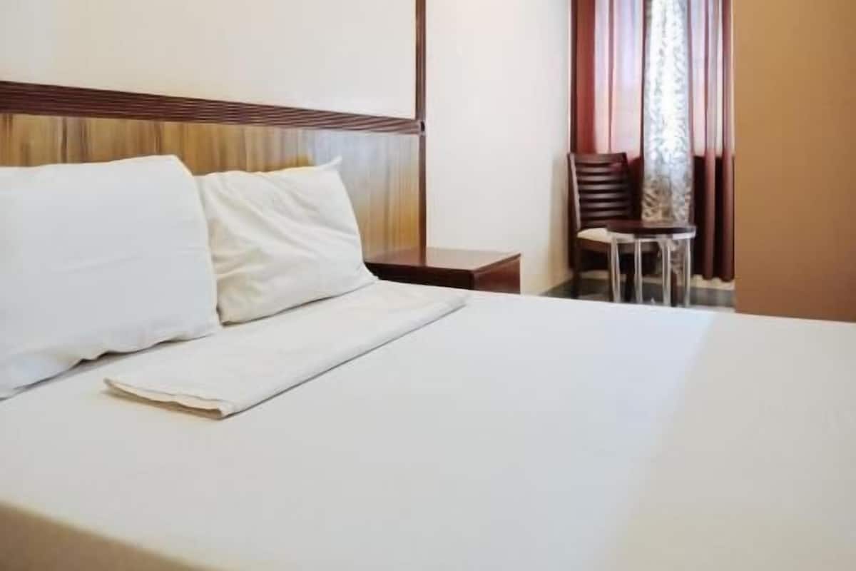 A hotel room with a bed, a nightstand, a chair, and a window with curtains.