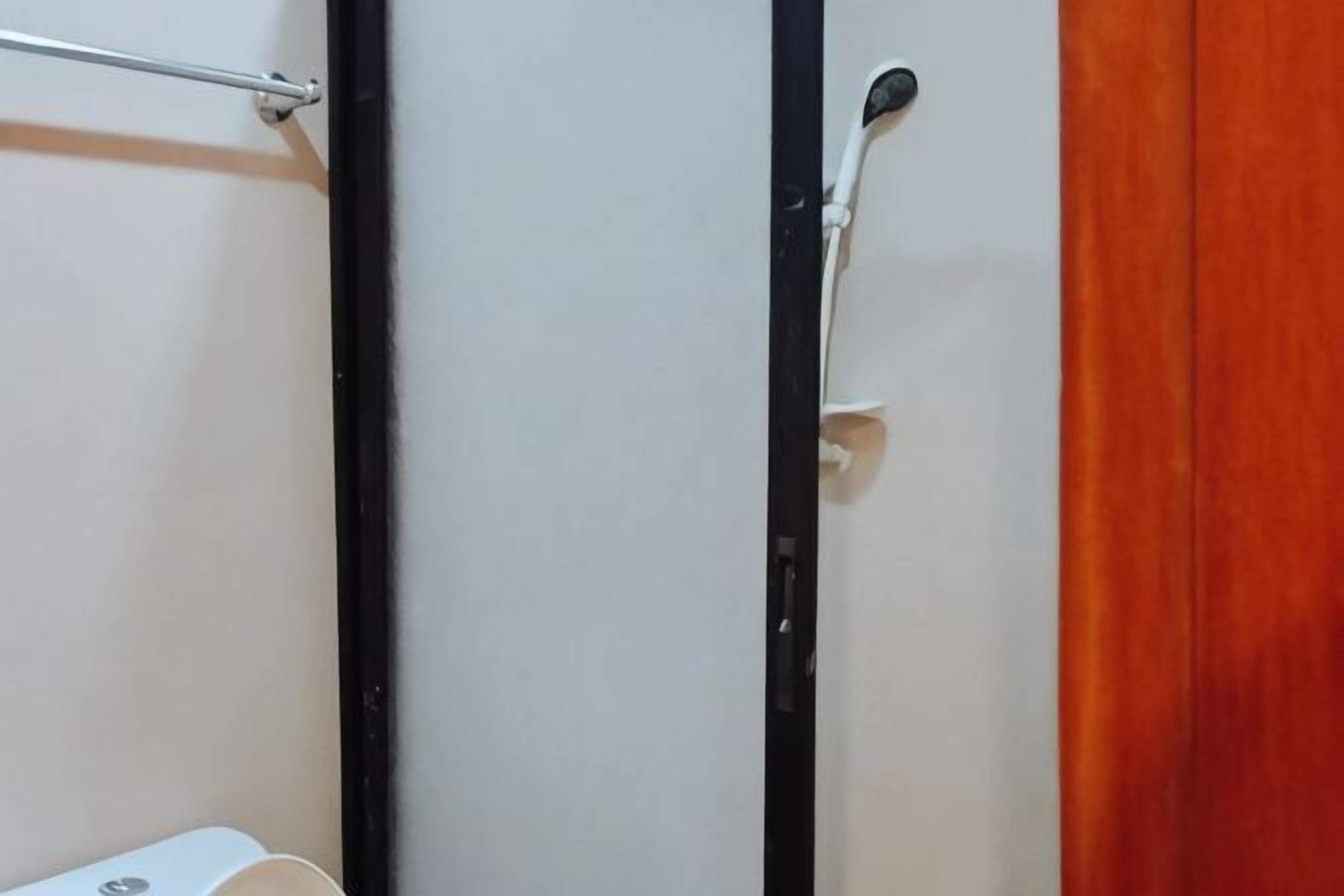 A bathroom with a white wall, a black door frame, and a wooden door.