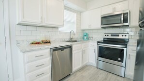Una cocina moderna con armarios blancos, lavavajillas de acero inoxidable, microondas integrado y horno doble.