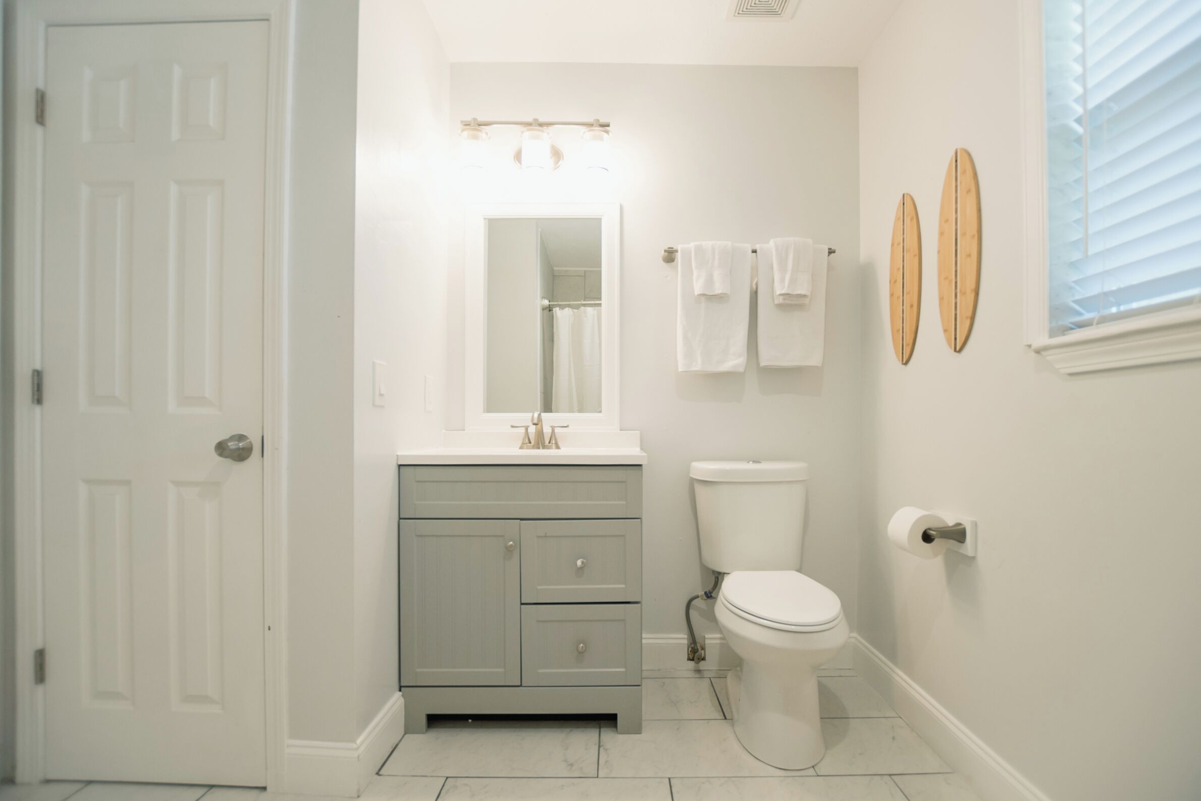 A bathroom with a white door, a vanity with a mirror, a toilet, and two towels hanging on the wall.