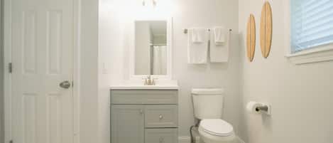 A bathroom with a white door, a vanity with a mirror, a toilet, and two towels hanging on the wall.
