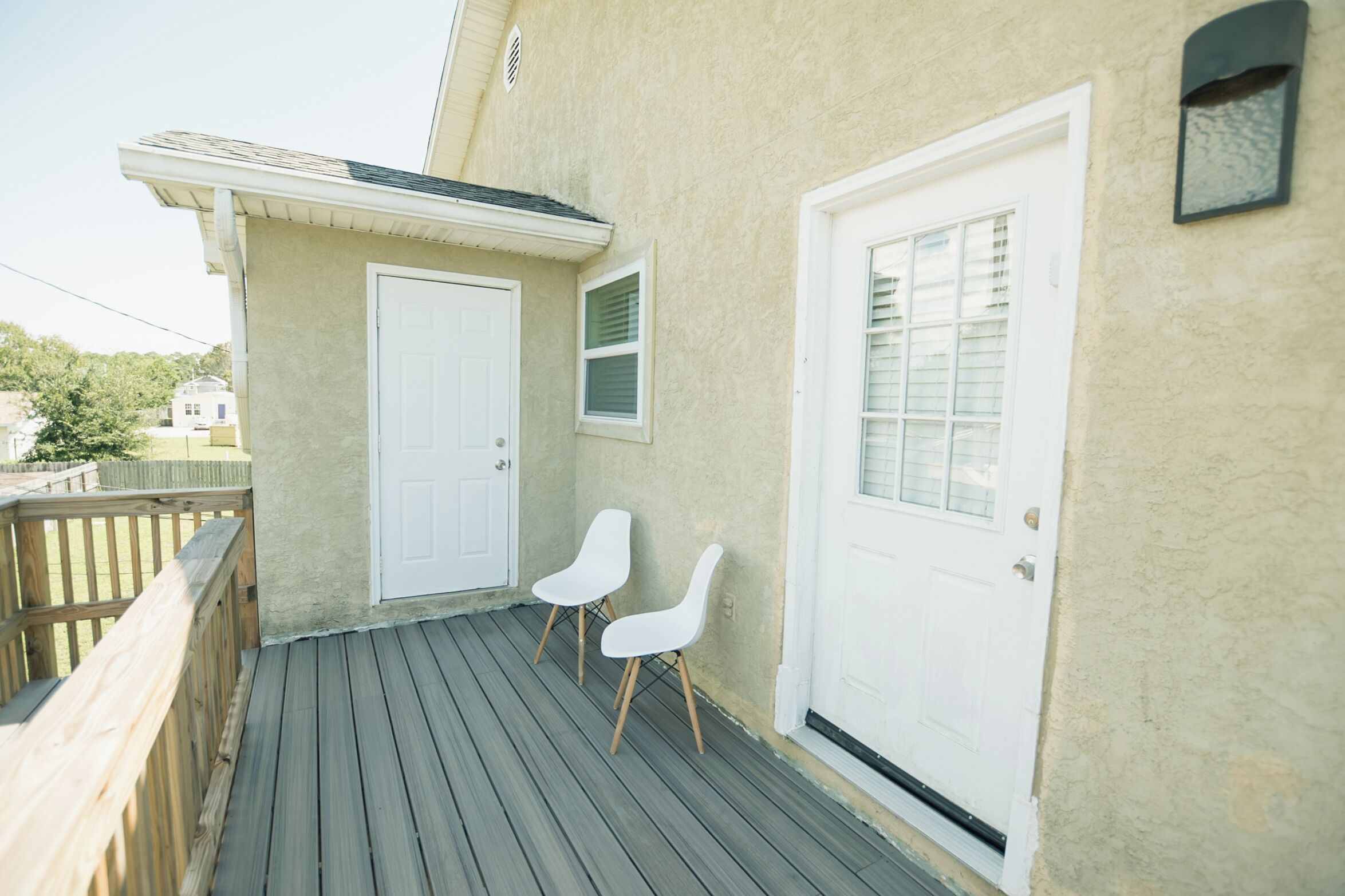 A wooden deck with two white chairs, a white door, and a small window with shutters.