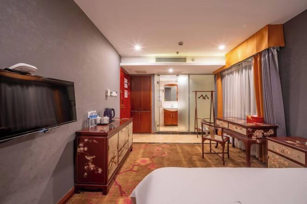 Camera d'albergo con un letto, una TV, una scrivania, una sedia, un armadio e un bagno visibile attraverso una porta aperta.
