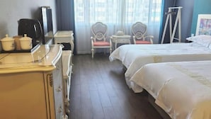 Een hotelkamer met twee bedden, een bureau met koffiezetapparaat, een stoel en een raam met gordijnen.