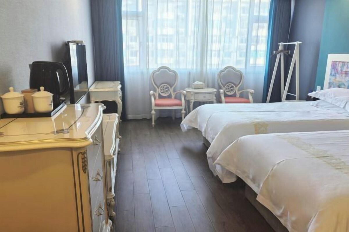 A hotel room with two beds, a desk with a coffee maker, a chair, and a window with curtains.