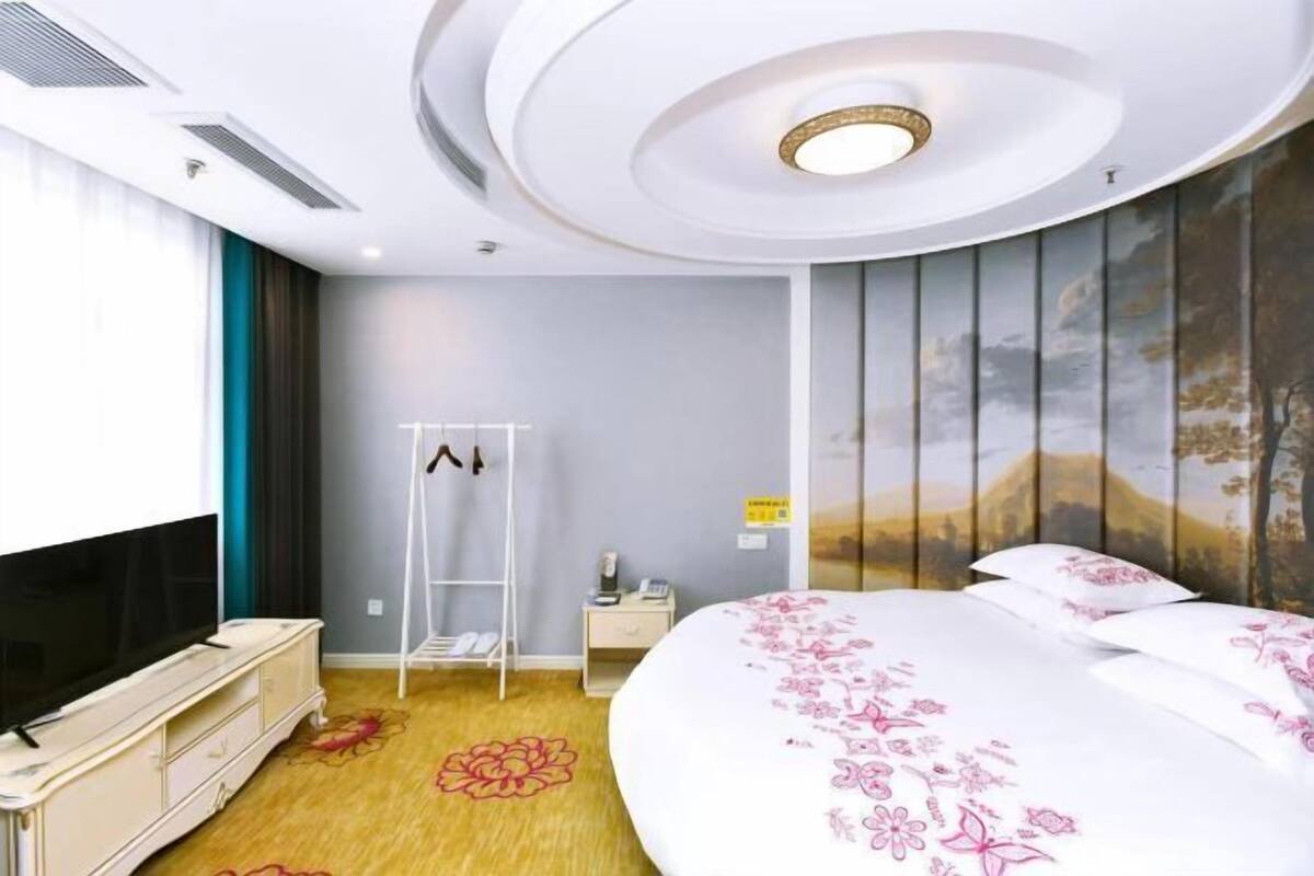 Camera d'albergo con un letto, una televisione, un portascarpe, un comodino e una parete decorata con un murale panoramico.