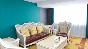 Een kamer met een blauwgroene accentmuur, twee witte gestoffeerde banken met gele kussens met een patroon, een witte salontafel en een vloerkleed met een ontwerp.