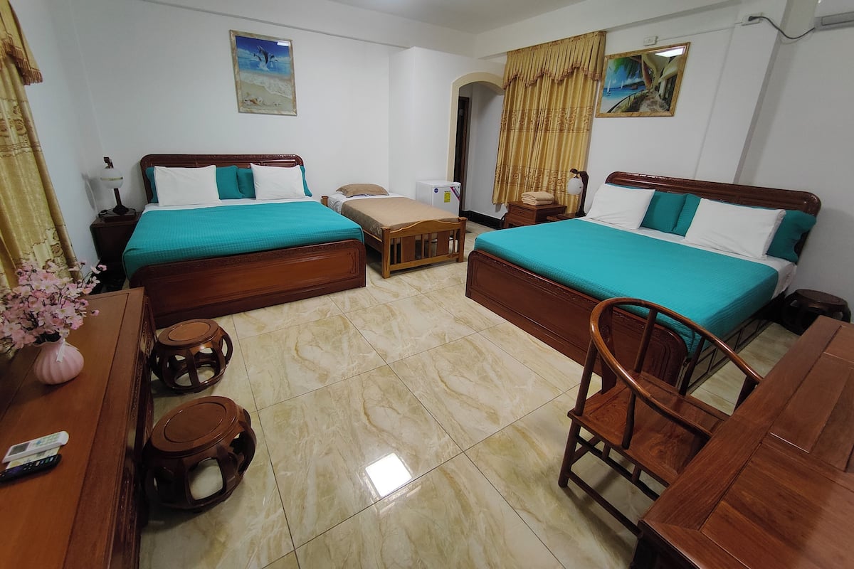 A hotel room with two wooden beds, a wooden desk, a chair, a small table, and a nightstand.