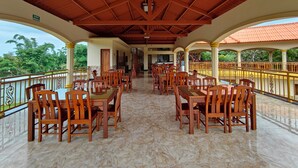 A covered outdoor dining area with wooden tables and chairs, a tiled floor, and a view of greenery. - Hotel Pacific Pearl (Punta Mala)