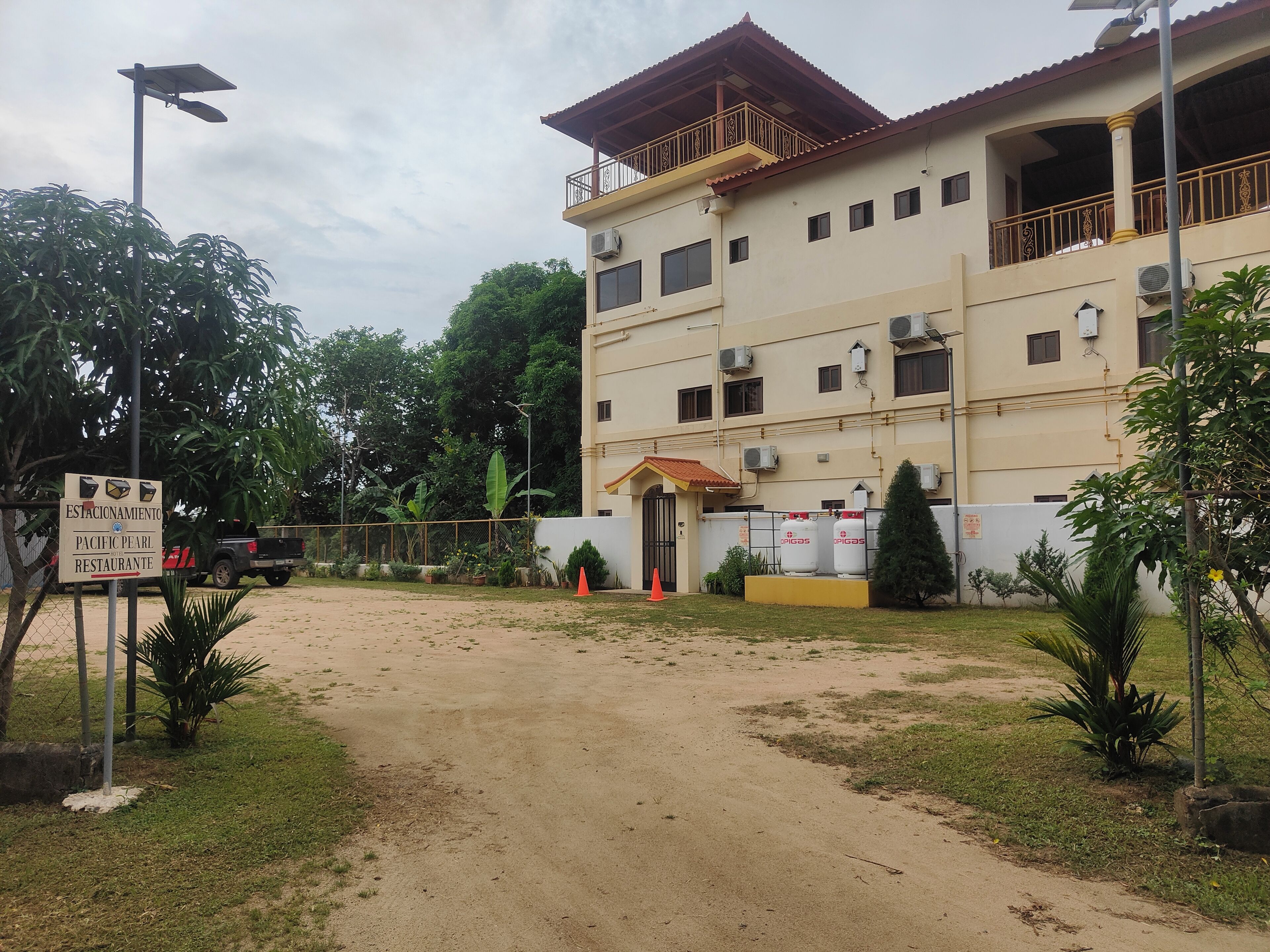A building with a sign for Pacific Pearl Restaurant, a dirt path leading to the entrance, and several air conditioning units on the exterior.