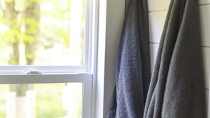 Una ventana con vistas a la vegetación, un perchero con toallas dobladas y una pared blanca.