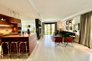 Una cocina moderna con barra, un comedor con sofá verde y vistas al exterior a través de un ventanal.