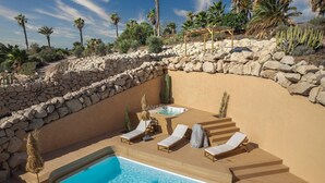 Una piscina con lettini, una vasca idromassaggio e un muro in pietra.