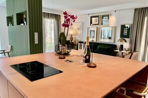 Una cocina moderna con placa de inducción, una mesa de comedor con sillas, un sofá verde y una planta ornamental de orquídea.