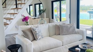 A modern living room with a white sofa, a wooden staircase, and a view of a pool.