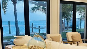 A modern living room with a view of the ocean, a wooden table with decorative items, and a sofa with cushions.