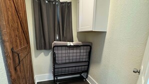 Un couloir étroit avec une porte en bois, un étagère en métal, une armoire blanche et une fenêtre avec des rideaux.