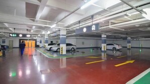 A multi-level parking garage with clear directional arrows on the floor, a man walking towards an exit, and several parked cars. - Dalian Huafa New Town Hotel Apartment (Dalian)