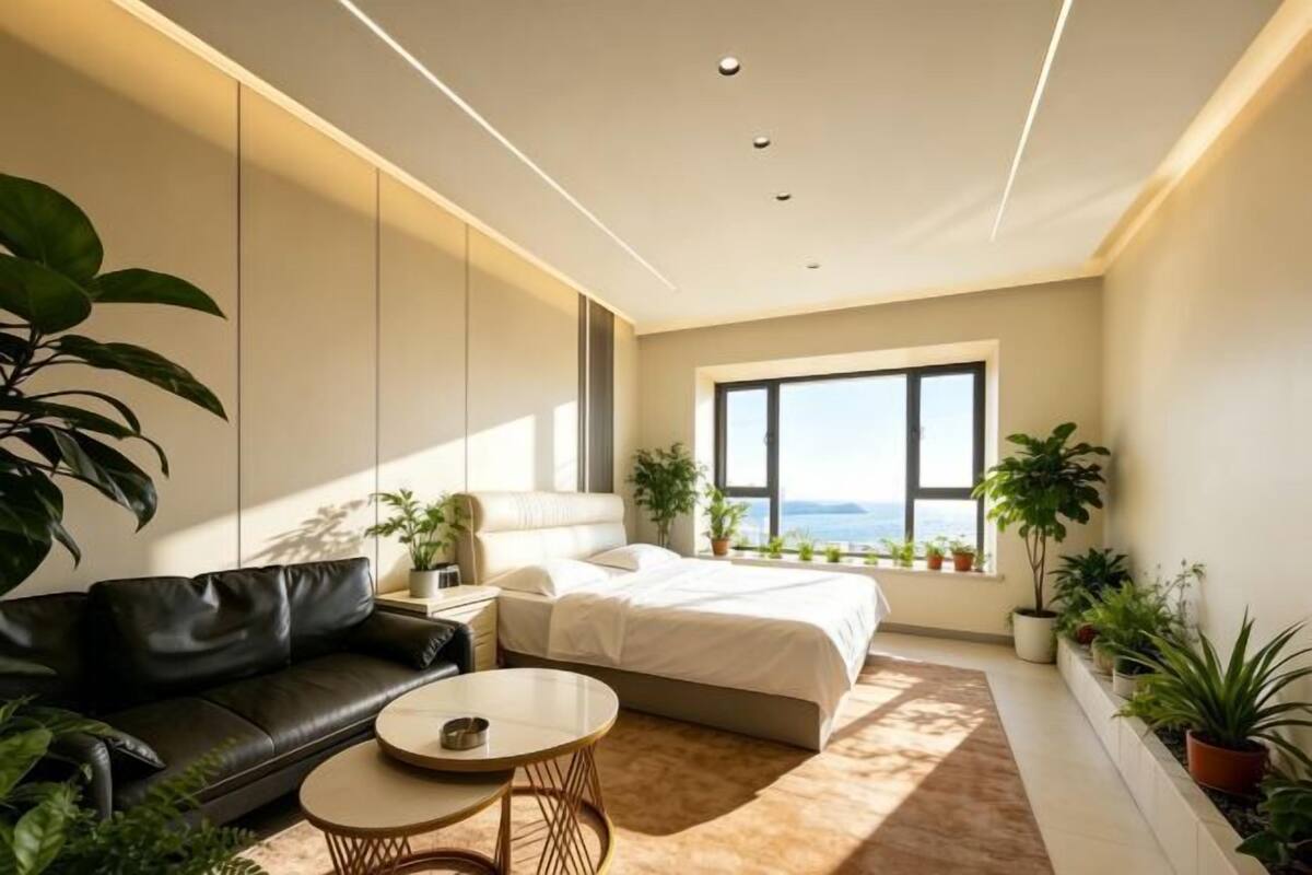 A modern bedroom with a bed, a sofa, a coffee table, and potted plants.