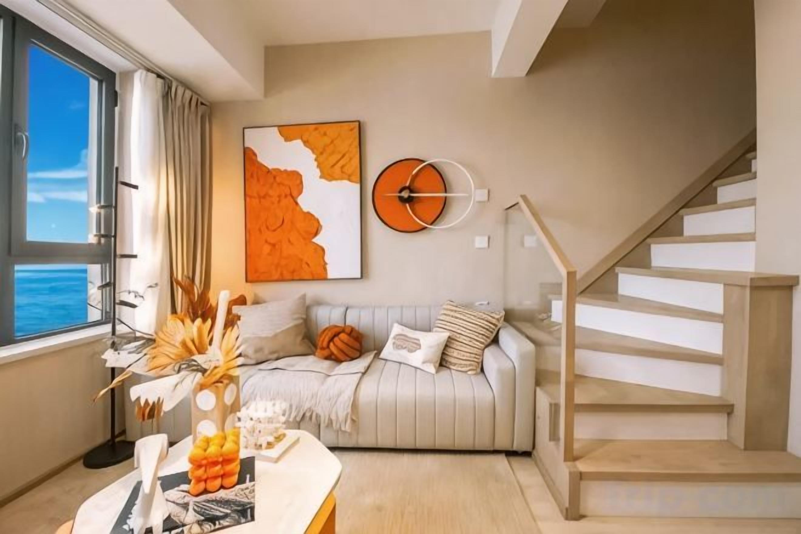 Una sala de estar moderna con un sofá, una mesa de centro con objetos decorativos, una escalera y un ventanal grande.
