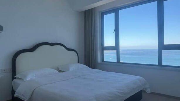 A bedroom with a large window, a bed, and a view of the sea. - Dalian Huafa New Town Hotel Apartment (Dalian)