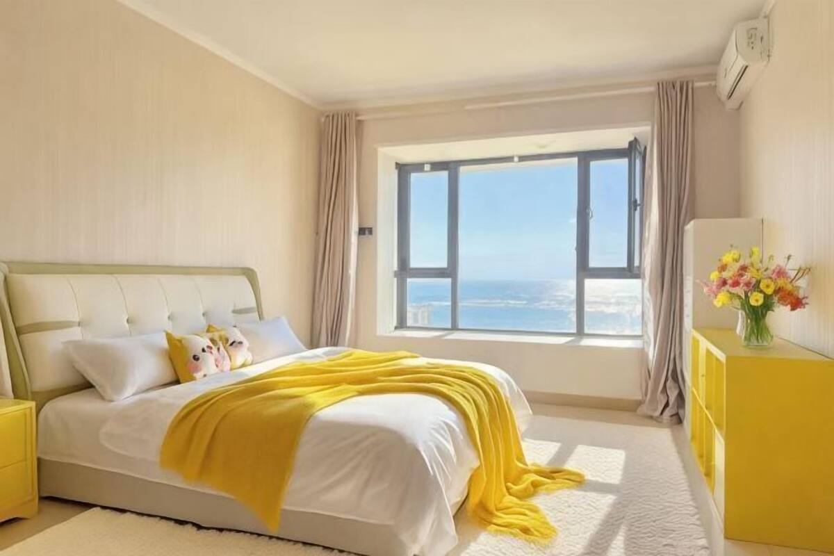 A bedroom with a bed, a window with curtains, a bedside table, and a yellow dresser.