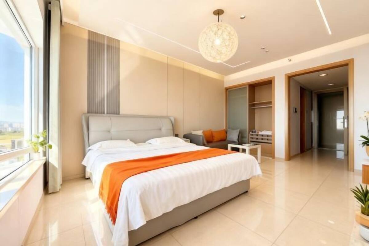 A modern hotel room with a large bed, a desk, a chair, and a view through the window.