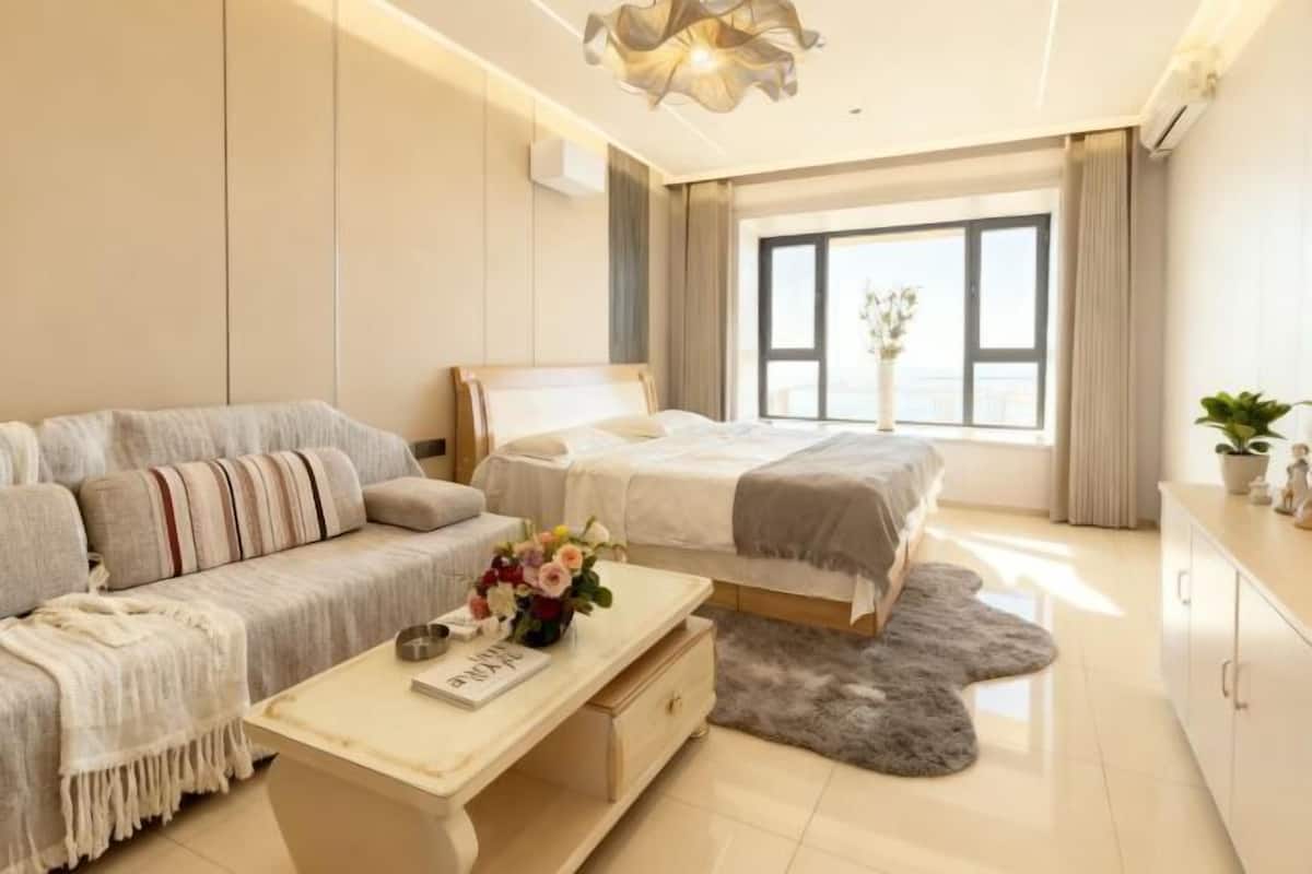 A modern bedroom with a sofa, a bed, a desk, and a view of the outside.