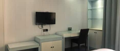 A hotel room with a bed, a desk, a chair, a TV, and a wardrobe.