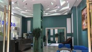Vestíbulo de hotel con mostrador de recepción, zona de estar y una planta grande en maceta.