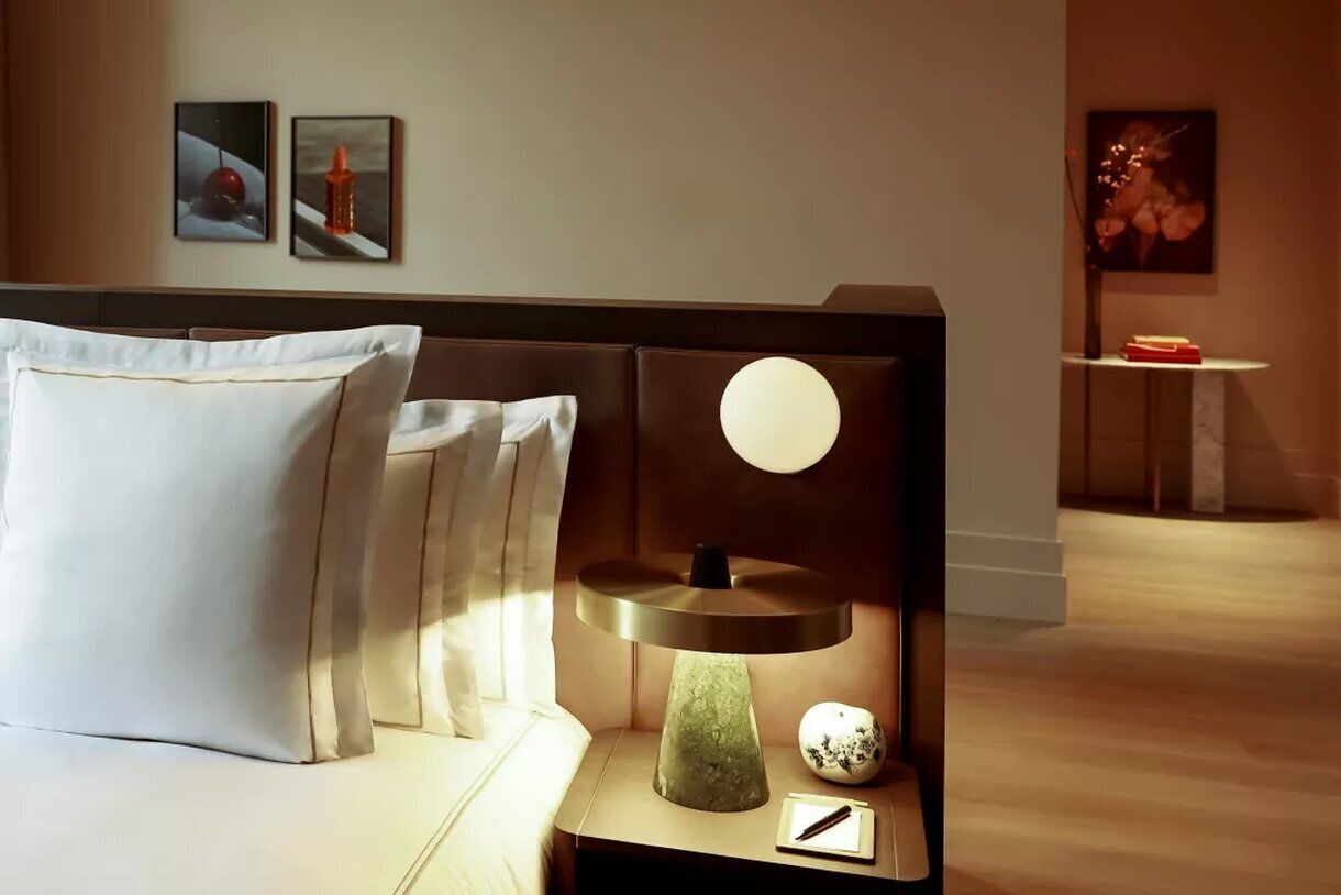 A hotel room with a bed, a bedside table with a lamp, and artwork on the walls.
